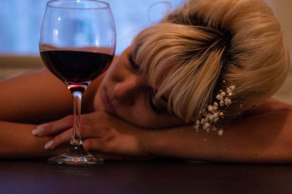 Woman With White Flower-accent Headdress Leaning Her Head on Table Beside Half-filled Wine Glass