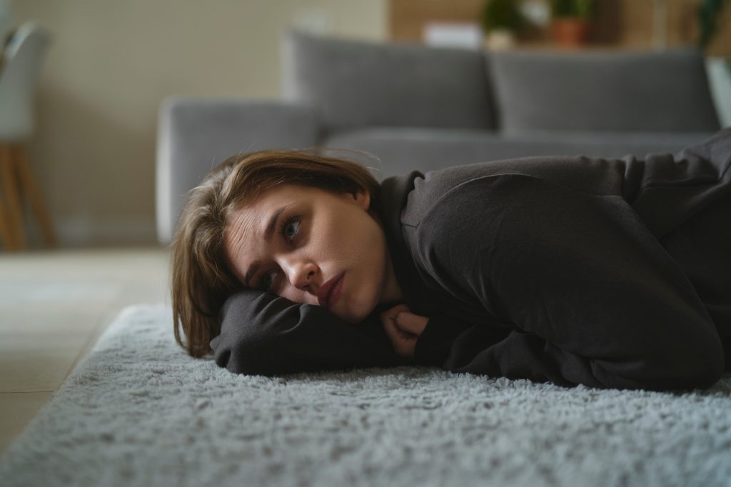 Caucasian woman lying down at the carpet in home with mental problem