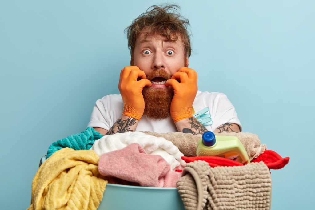 Frustrated neurotic overworked foxy man looks through peal of dirty clothes, bites finger nails, wor