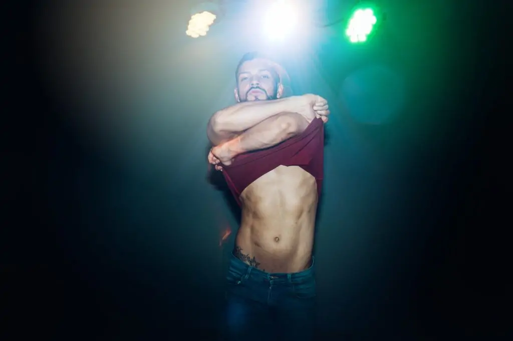 Muscular man undressing in lights while dancing