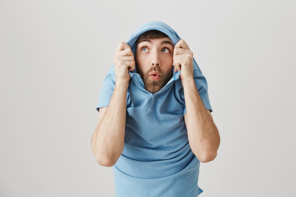 Positive funny european male pulling shirt on head and staring through collar up as if seeing some