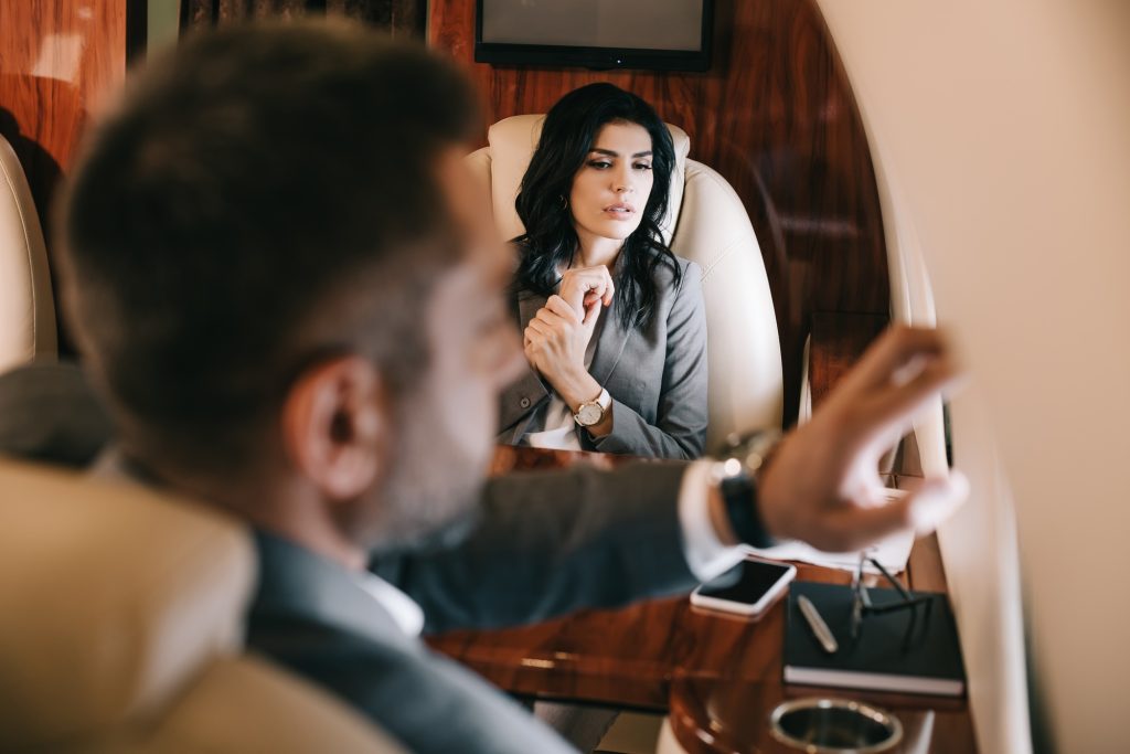 selective focus of worried businesswoman with fear of flight sitting with businessman in private jet