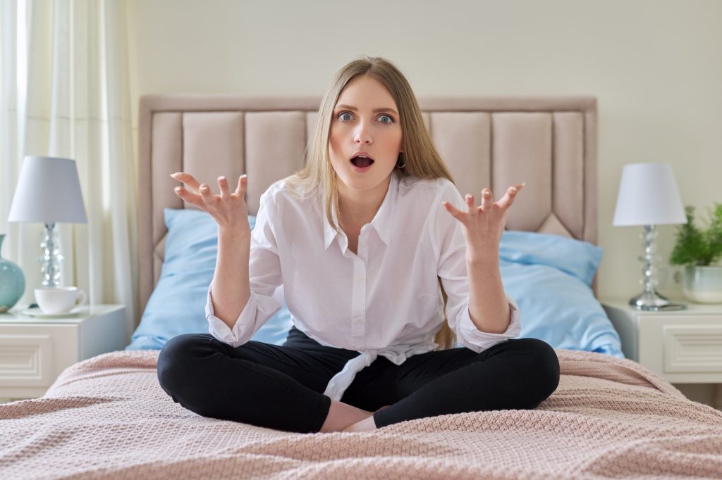 Serious anxious worried young woman sitting at home in bed