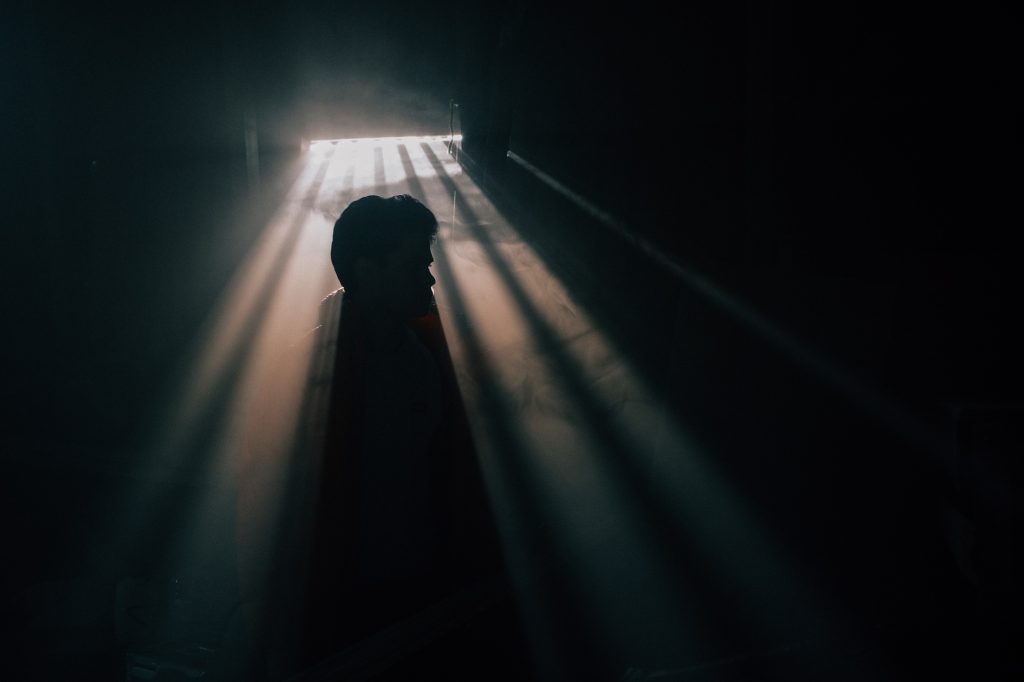 A man silhouetted against a window with sunshine pouring through in a dark room