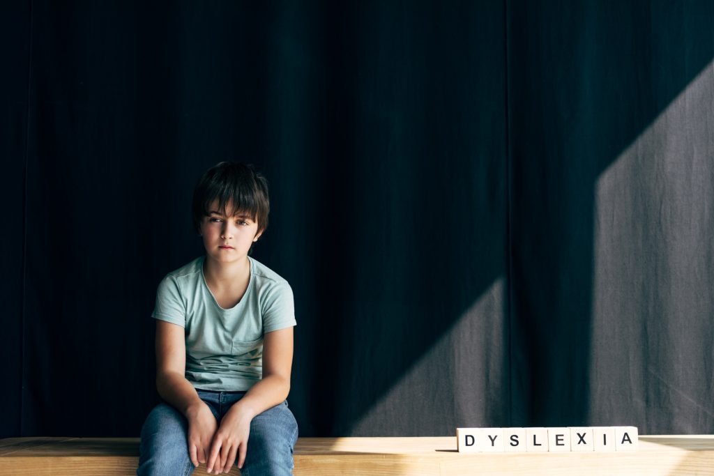 La dyslexie : un trouble à dépister dès le jeune âge kid with dyslexia looking at camera and sitting near wooden cubes with lettering dyslexia