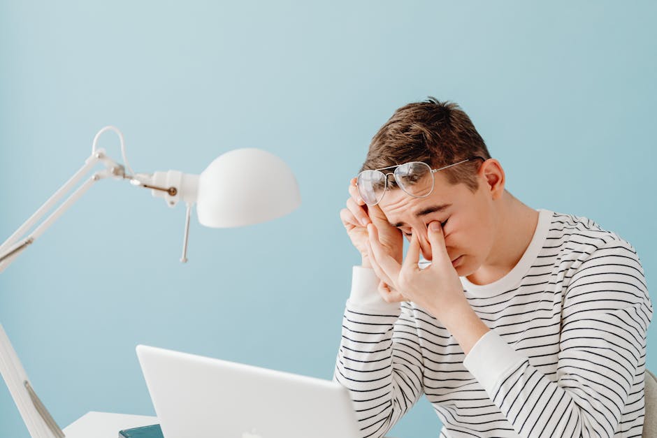 Person rubbing eyes in front of a computer screen with headache and fatigue