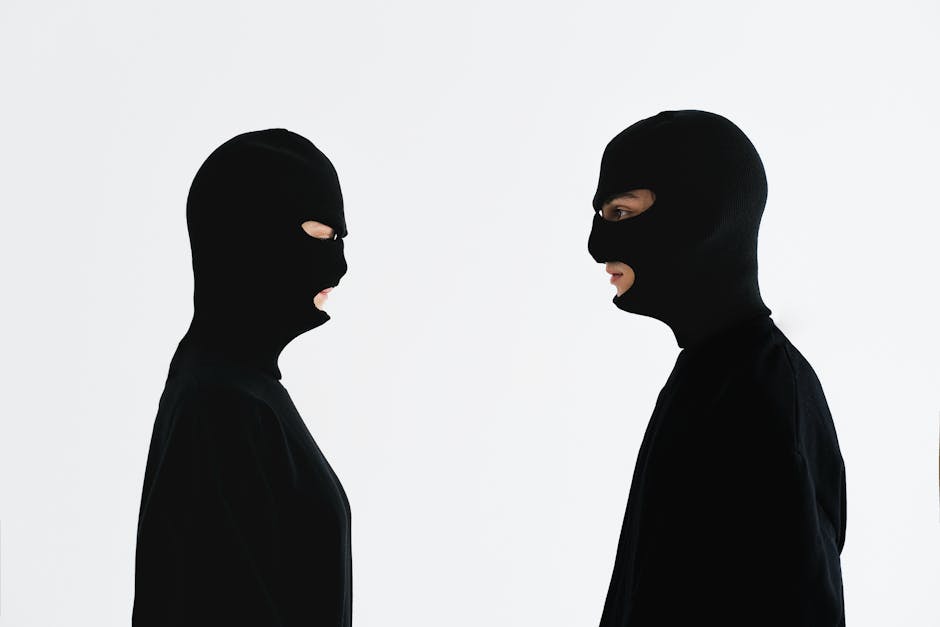 Psychologie du conflit constructif : l’art de la confrontation saine Two individuals in black balaclavas facing each other against a white background.